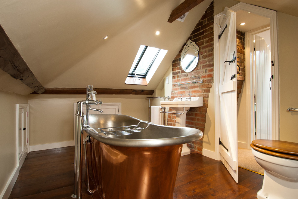 Design ideas for a country bathroom in Surrey with a pedestal sink, a freestanding tub, beige walls and dark hardwood floors.