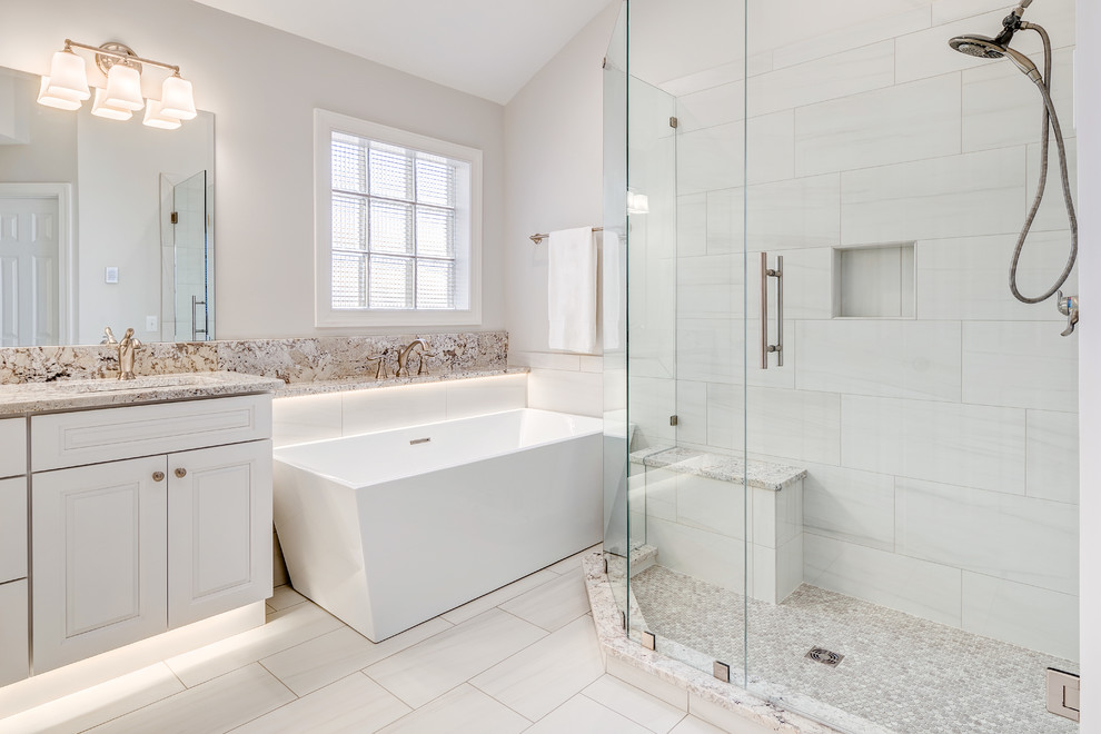 Freestanding bathtub - large transitional master gray tile and porcelain tile porcelain tile and gray floor freestanding bathtub idea with raised-panel cabinets, white cabinets, a two-piece toilet, gray walls, an undermount sink, granite countertops and a hinged shower door