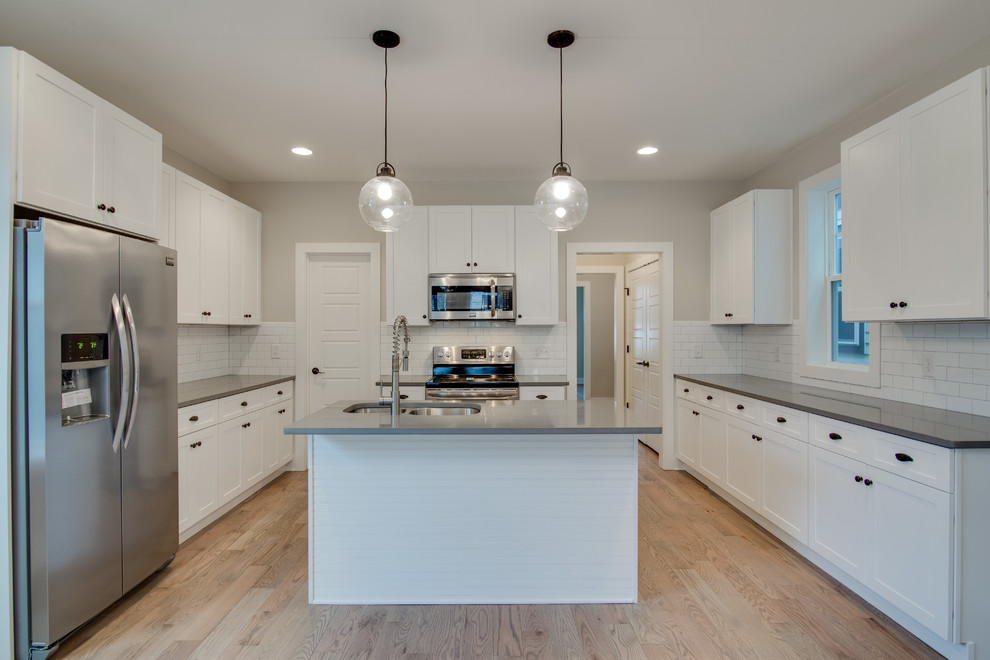 Mid-sized traditional u-shaped eat-in kitchen in Nashville with a double-bowl sink, white cabinets, quartzite benchtops, white splashback, stainless steel appliances, light hardwood floors and with island.