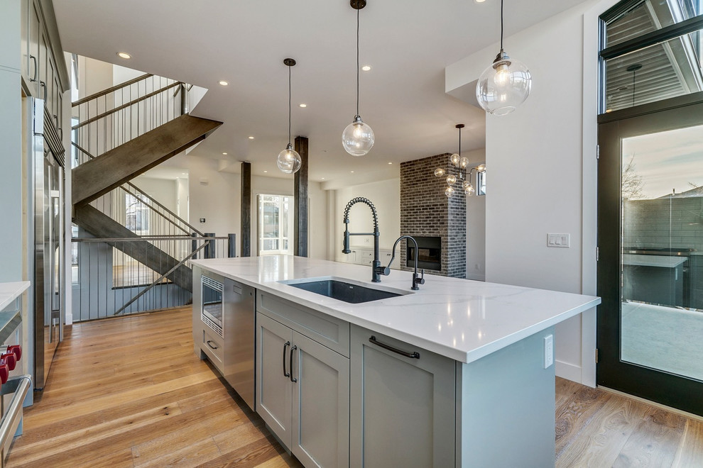 Inspiration for a mid-sized transitional l-shaped medium tone wood floor and brown floor eat-in kitchen remodel in Calgary with a single-bowl sink, shaker cabinets, gray cabinets, quartzite countertops, white backsplash, ceramic backsplash, stainless steel appliances, an island and white countertops