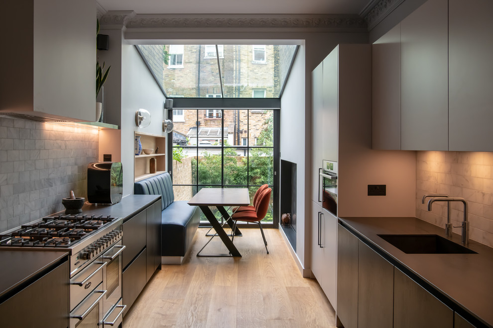 Design ideas for a mid-sized contemporary galley eat-in kitchen in London with flat-panel cabinets, black cabinets, grey splashback, stainless steel appliances, light hardwood floors, no island, beige floor, black benchtop, a single-bowl sink and marble splashback.