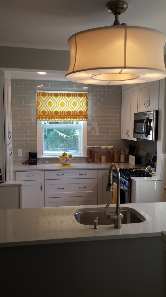 Example of a small transitional u-shaped light wood floor enclosed kitchen design in New York with an undermount sink, shaker cabinets, white cabinets, solid surface countertops, gray backsplash, subway tile backsplash and stainless steel appliances