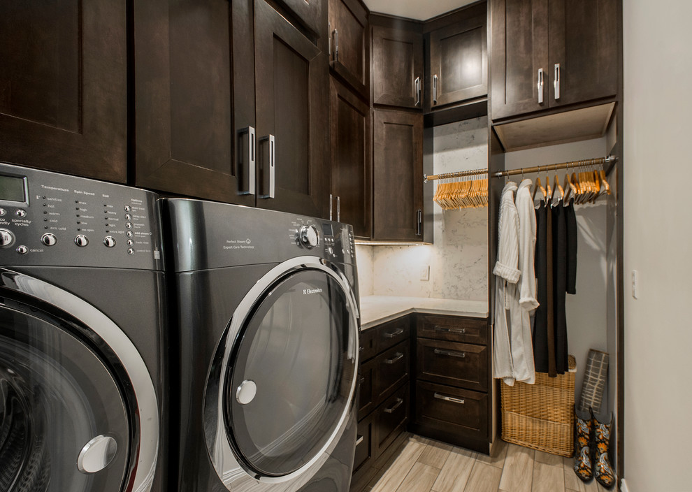 Mid-sized transitional l-shaped dedicated laundry room in Dallas with shaker cabinets, dark wood cabinets, quartzite benchtops, grey walls, porcelain floors and a side-by-side washer and dryer.