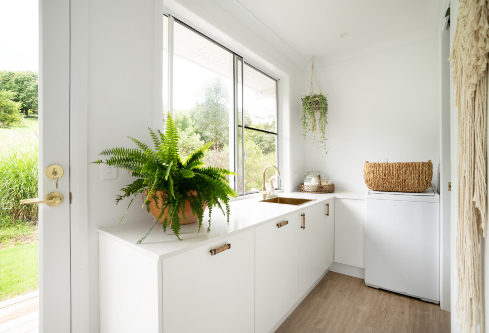 This is an example of a contemporary l-shaped dedicated laundry room in Sunshine Coast with a drop-in sink, flat-panel cabinets, quartz benchtops, white walls, vinyl floors, beige floor and white benchtop.
