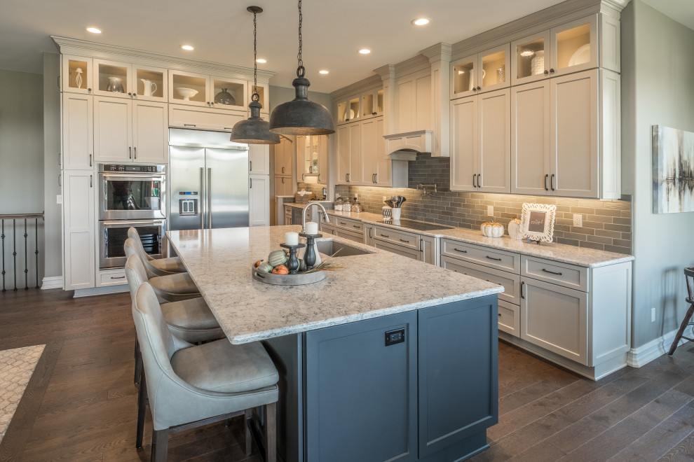 Inspiration for a large country l-shaped open plan kitchen in Detroit with an undermount sink, recessed-panel cabinets, beige cabinets, grey splashback, stainless steel appliances, dark hardwood floors, with island, brown floor and multi-coloured benchtop.