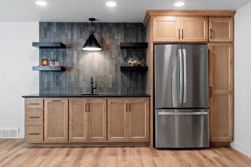 Inspiration for a large transitional single-wall vinyl floor and brown floor wet bar remodel with an undermount sink, shaker cabinets, brown cabinets, quartzite countertops, black backsplash, porcelain backsplash and black countertops