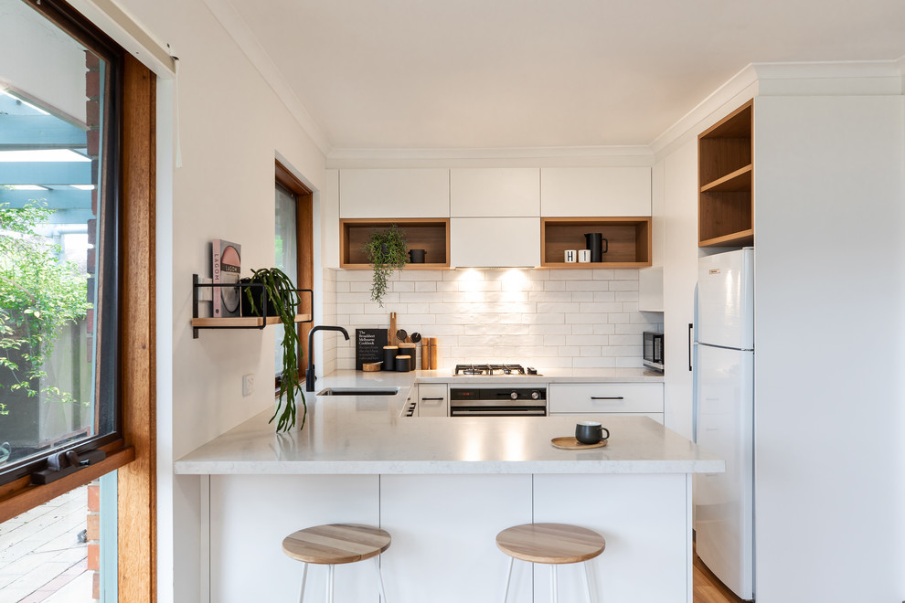 Contemporary u-shaped kitchen in Adelaide with an undermount sink, flat-panel cabinets, white cabinets, white splashback, white appliances, a peninsula, brown floor, white benchtop and laminate floors.