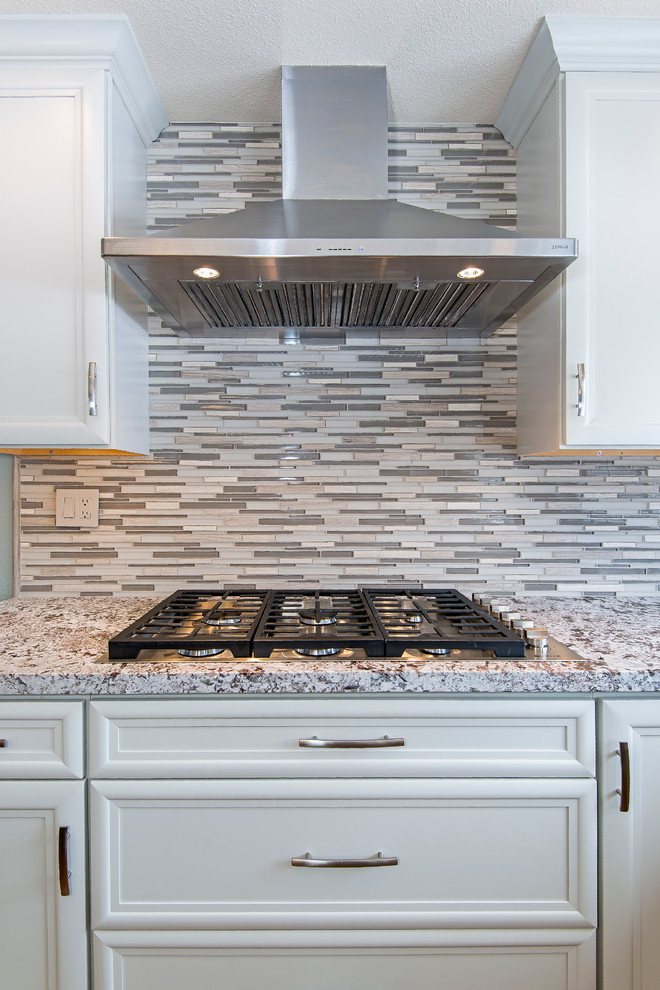 Example of a large transitional medium tone wood floor enclosed kitchen design with a farmhouse sink, recessed-panel cabinets, white cabinets, granite countertops, multicolored backsplash, matchstick tile backsplash, stainless steel appliances and an island