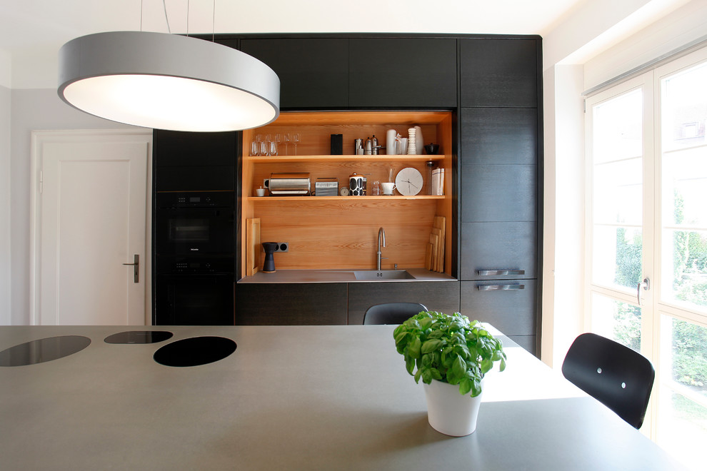Design ideas for a mid-sized contemporary separate kitchen in Nuremberg with flat-panel cabinets, dark wood cabinets, concrete benchtops, black appliances, light hardwood floors, with island, grey benchtop, a single-bowl sink and timber splashback.