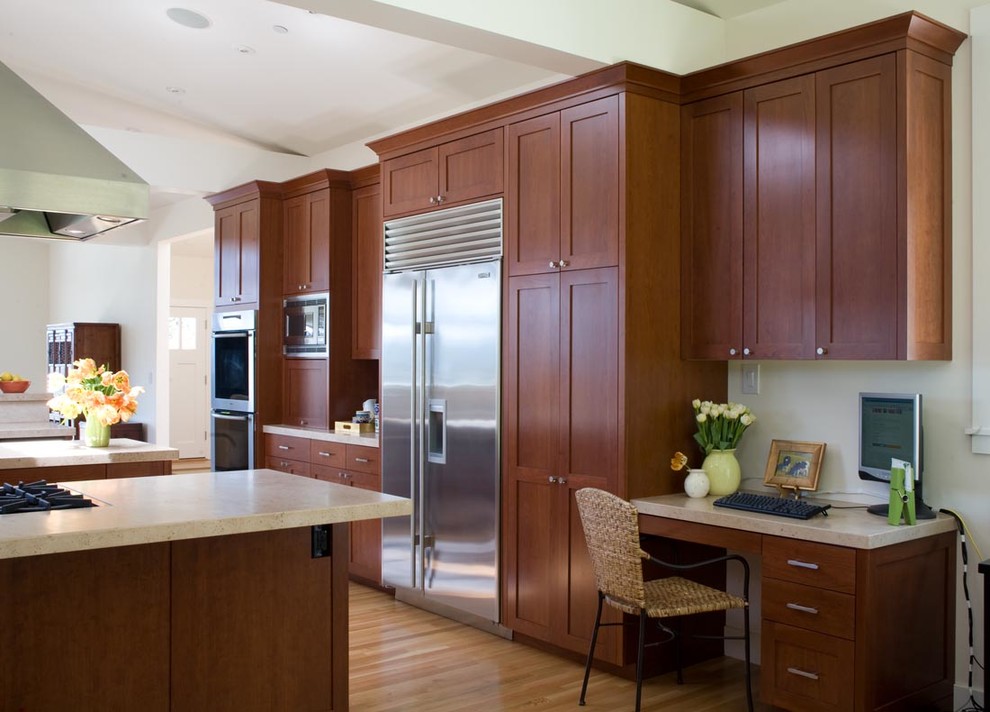 This is an example of a mid-sized u-shaped eat-in kitchen in San Francisco with an undermount sink, shaker cabinets, medium wood cabinets, limestone benchtops, beige splashback, stone tile splashback, stainless steel appliances, light hardwood floors, multiple islands and beige benchtop.
