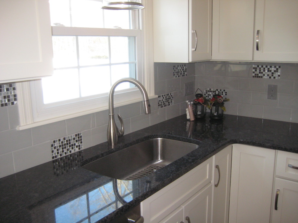 Example of a mid-sized transitional u-shaped medium tone wood floor and brown floor enclosed kitchen design in Boston with an undermount sink, shaker cabinets, white cabinets, granite countertops, gray backsplash, subway tile backsplash, stainless steel appliances and an island