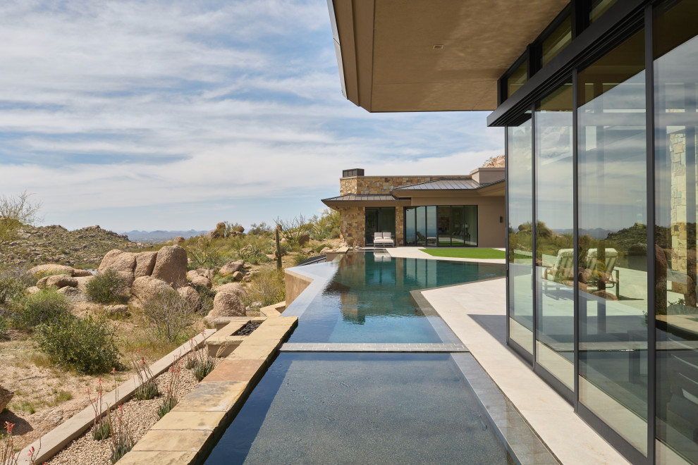 Expansive contemporary backyard custom-shaped infinity pool in Phoenix with with privacy feature and natural stone pavers.
