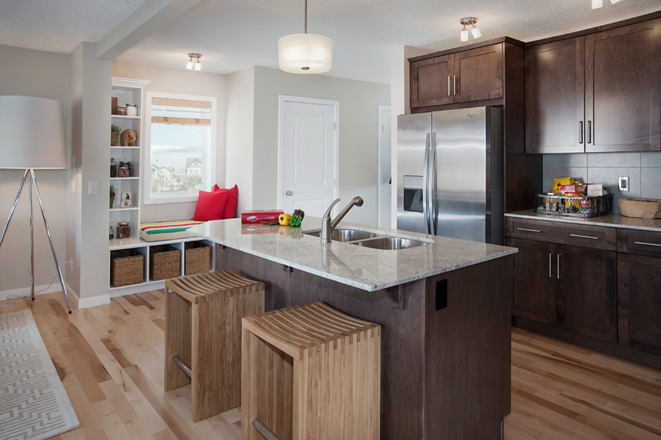 Example of a trendy l-shaped eat-in kitchen design in Calgary with a drop-in sink, dark wood cabinets, granite countertops, gray backsplash and stainless steel appliances