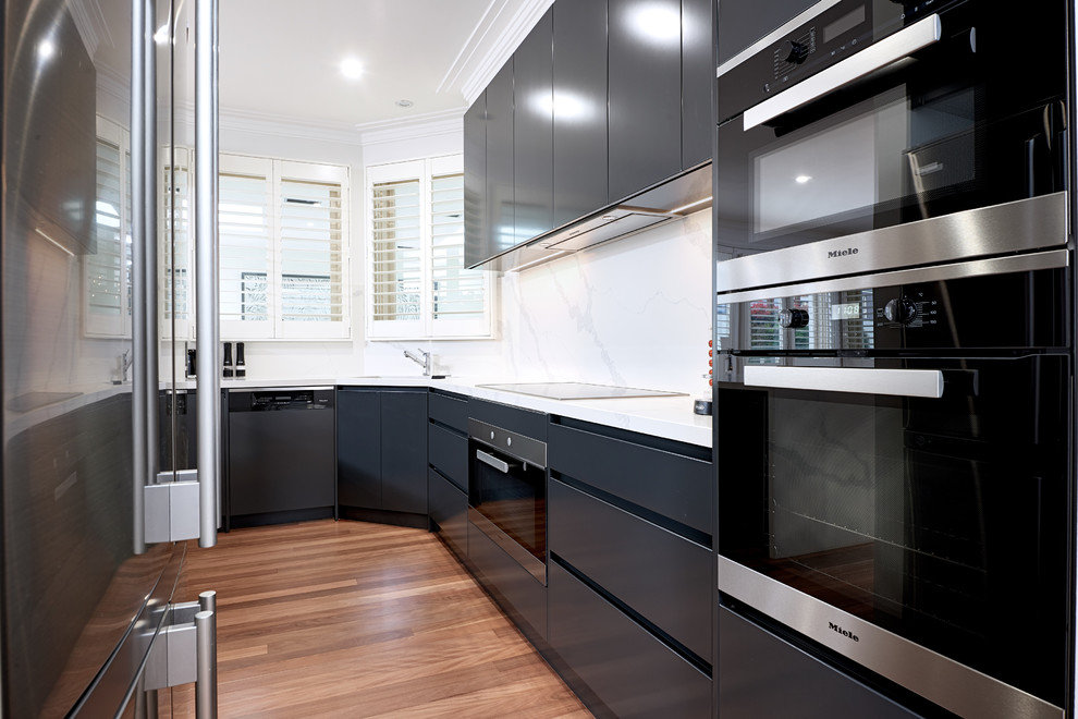 Inspiration for a mid-sized modern u-shaped kitchen pantry in Melbourne with an undermount sink, black cabinets, solid surface benchtops, white splashback, stone slab splashback, stainless steel appliances, light hardwood floors, brown floor and white benchtop.