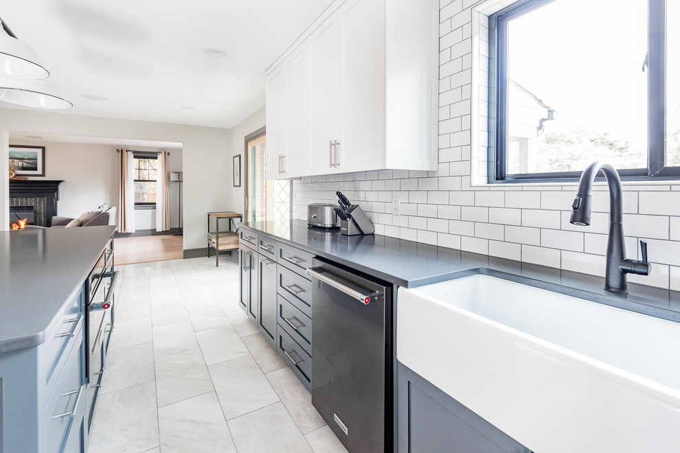 Large country l-shaped separate kitchen in Wilmington with a farmhouse sink, shaker cabinets, blue cabinets, quartz benchtops, white splashback, subway tile splashback, black appliances, marble floors, with island, grey floor and black benchtop.