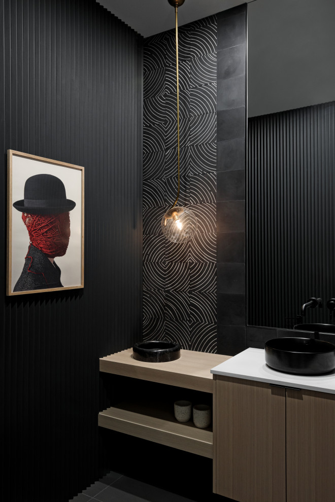 This is an example of a mid-sized modern powder room in Vancouver with flat-panel cabinets, light wood cabinets, black walls, a vessel sink, grey floor, white benchtops, a floating vanity and panelled walls.