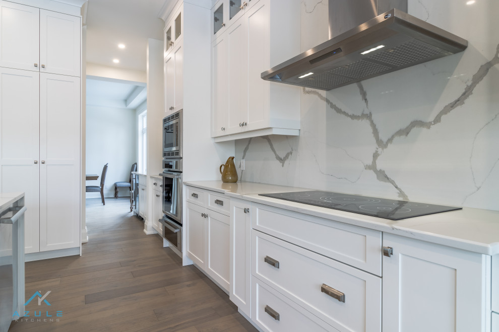Inspiration for a large transitional medium tone wood floor and multicolored floor kitchen remodel with an undermount sink, shaker cabinets, white cabinets, quartz countertops, white backsplash, quartz backsplash, stainless steel appliances, an island and white countertops