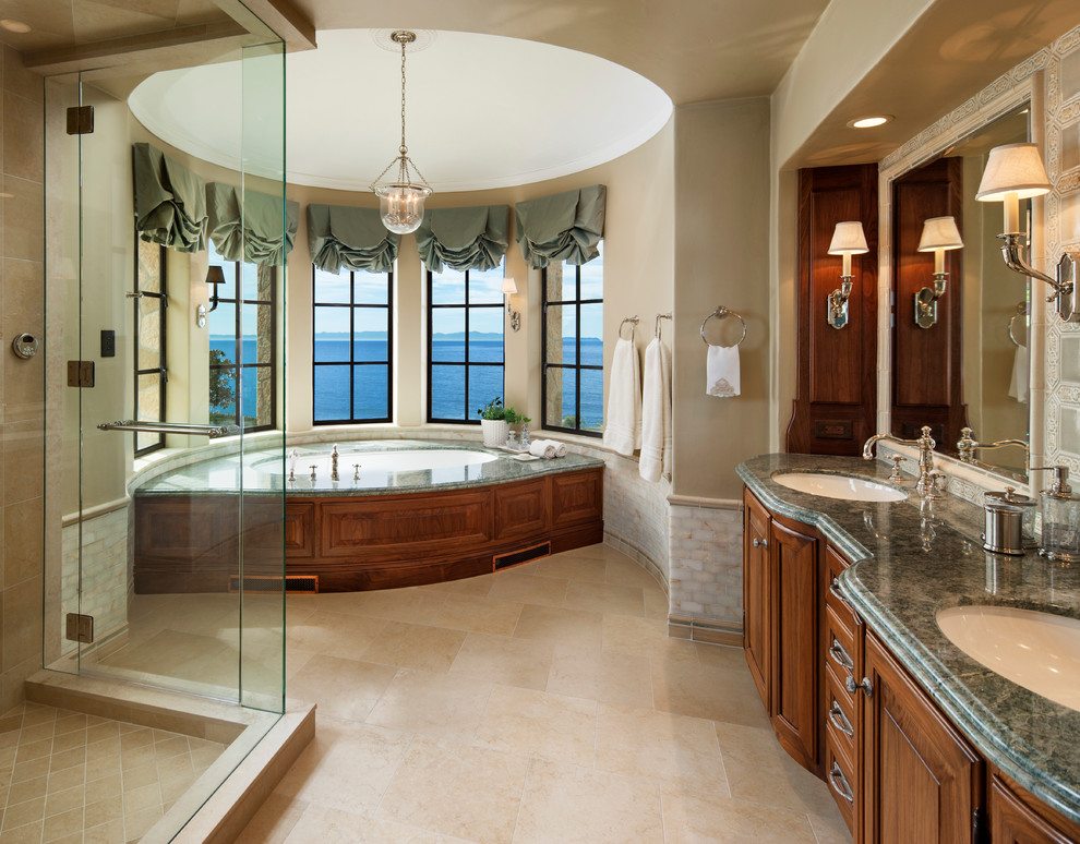 Photo of a large traditional master bathroom in Santa Barbara with raised-panel cabinets, medium wood cabinets, an undermount tub, beige walls, an undermount sink, beige floor, a corner shower, beige tile, porcelain tile, travertine floors, granite benchtops, a hinged shower door and green benchtops.