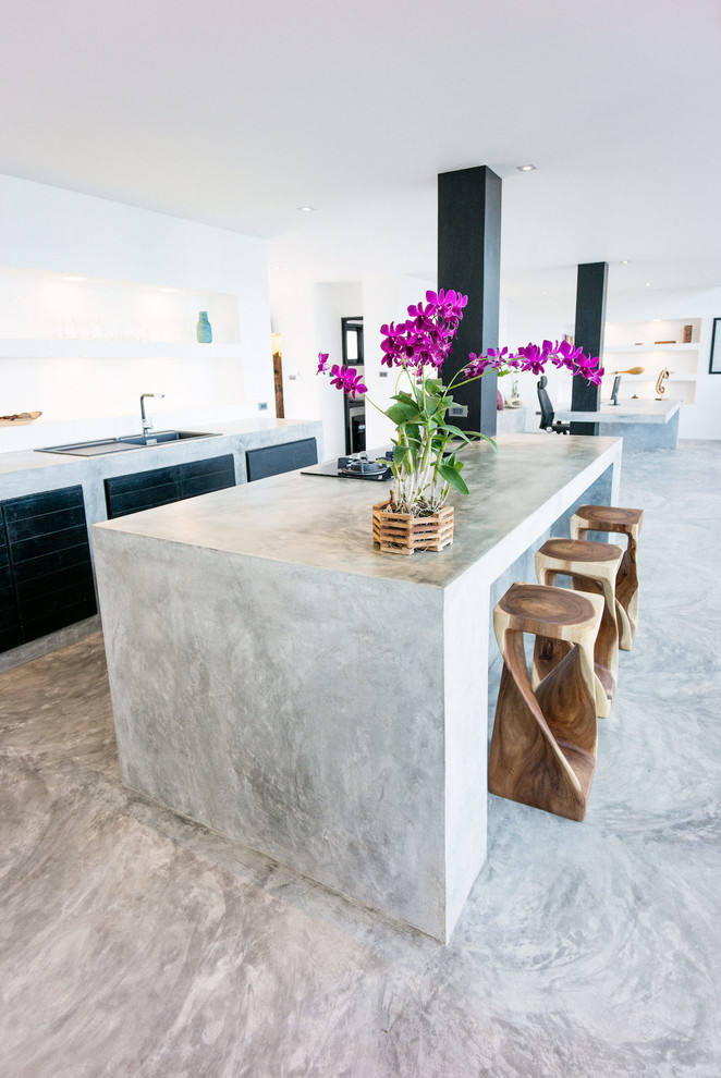 Mid-sized beach style single-wall open plan kitchen in Other with a drop-in sink, flat-panel cabinets, dark wood cabinets, concrete benchtops, white splashback, limestone splashback, panelled appliances, concrete floors, with island, grey floor and grey benchtop.