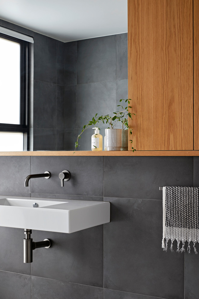 Photo of a large modern master bathroom in Melbourne with flat-panel cabinets, light wood cabinets, a freestanding tub, an open shower, a one-piece toilet, gray tile, porcelain tile and a wall-mount sink.