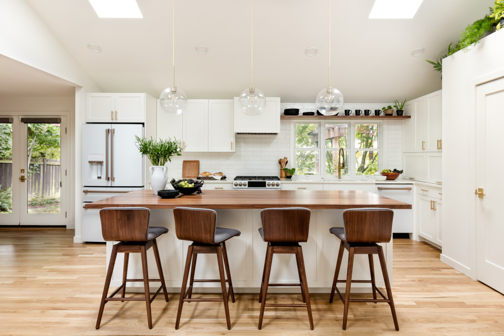 This is an example of a mid-sized scandinavian l-shaped eat-in kitchen in Seattle with an undermount sink, recessed-panel cabinets, white cabinets, quartz benchtops, white splashback, subway tile splashback, white appliances, light hardwood floors, with island, white benchtop and vaulted.