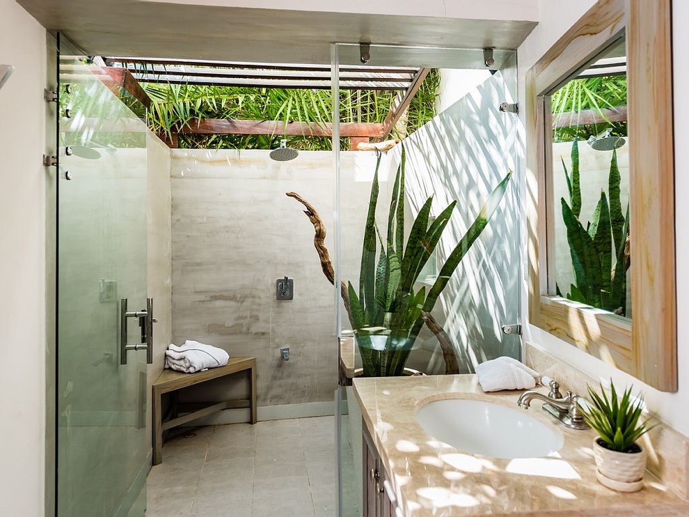 Photo of a tropical wet room bathroom in Other with dark wood cabinets, gray tile, white walls, an undermount sink, grey floor, a hinged shower door and beige benchtops.
