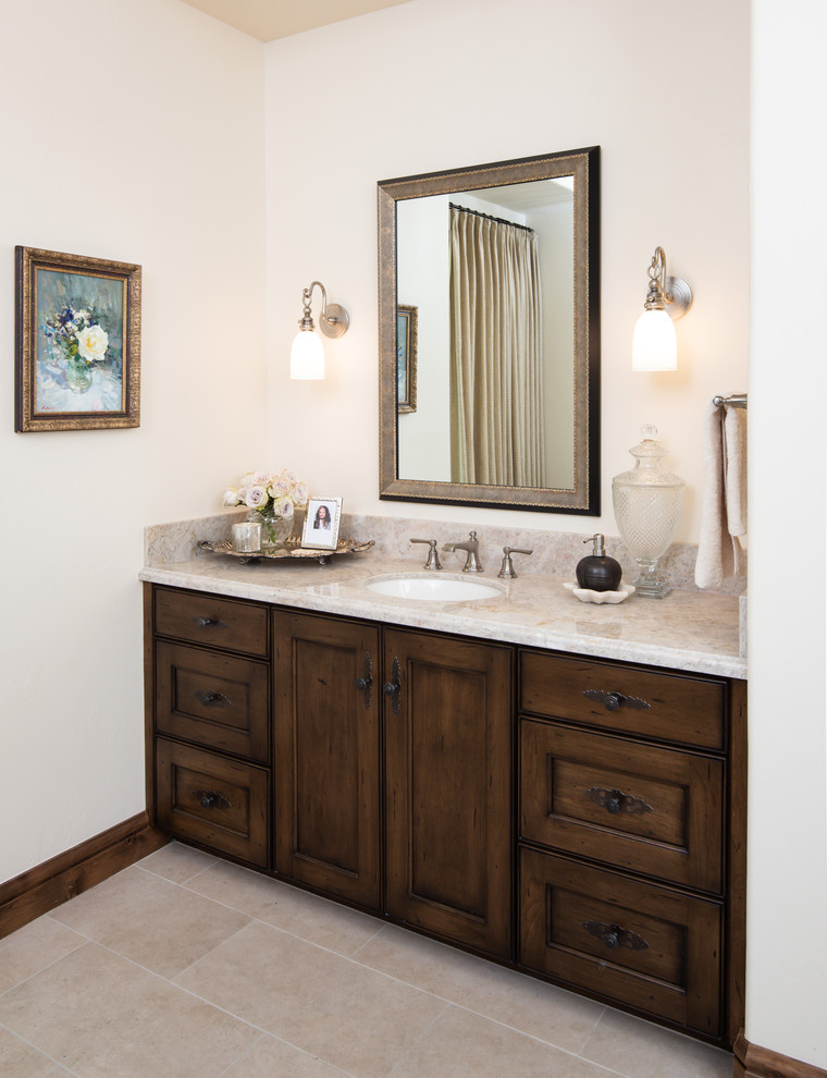 Photo of a large mediterranean master bathroom in Phoenix with recessed-panel cabinets, dark wood cabinets, a freestanding tub, beige walls, an undermount sink, quartzite benchtops, beige benchtops, limestone floors and beige floor.