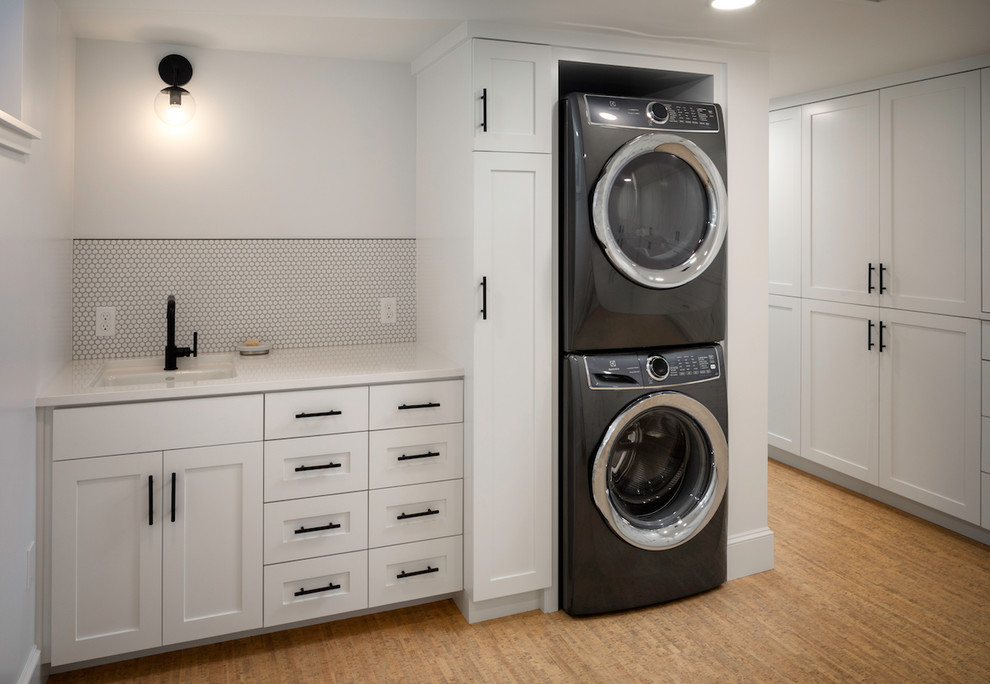 This is an example of a mid-sized modern single-wall utility room in Portland with an undermount sink, recessed-panel cabinets, white cabinets, quartz benchtops, white walls, light hardwood floors, a stacked washer and dryer, beige floor and white benchtop.