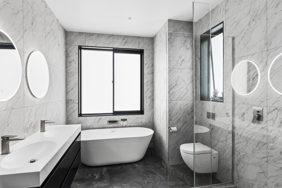 Свежая идея для дизайна: большая ванная комната с черными фасадами, отдельно стоящей ванной, угловым душем, инсталляцией, черно-белой плиткой, мраморной плиткой, бетонным полом, монолитной раковиной, серым полом, белой столешницей, тумбой под две раковины и подвесной тумбой - отличное фото интерьера