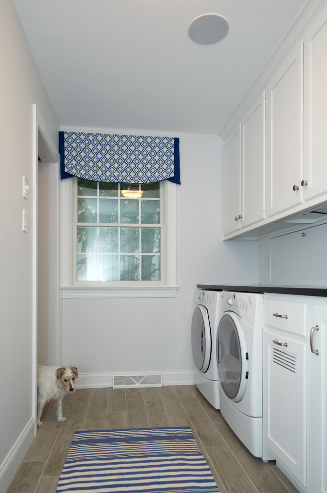 This is an example of a mid-sized transitional single-wall utility room in Philadelphia with an undermount sink, flat-panel cabinets, white cabinets, granite benchtops, white walls, ceramic floors and a side-by-side washer and dryer.