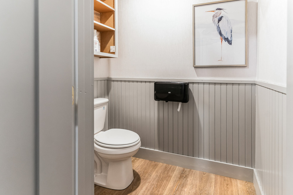 Powder room - large transitional vinyl floor, brown floor, vaulted ceiling and wainscoting powder room idea in Portland Maine with a one-piece toilet and white walls