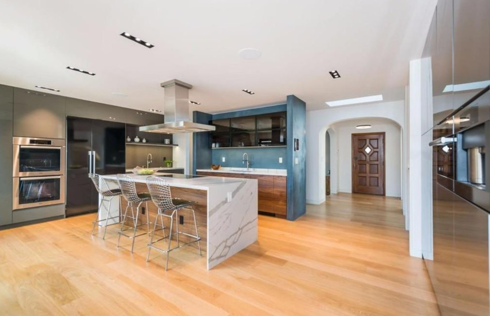 Large transitional l-shaped light wood floor open concept kitchen photo in Boston with an undermount sink, glass-front cabinets, black cabinets, marble countertops and an island