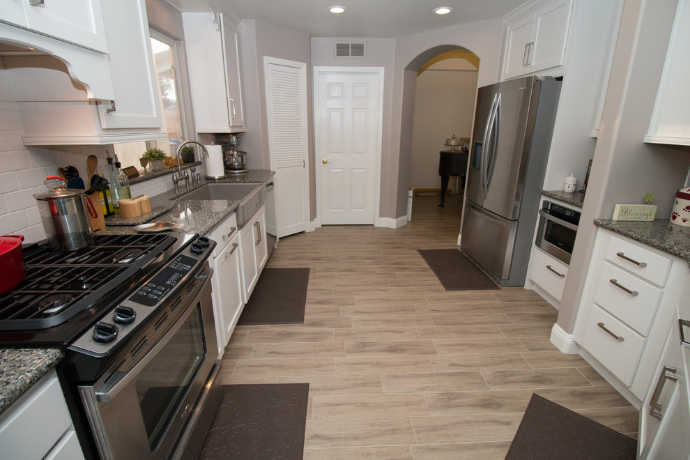 Inspiration for a mid-sized transitional galley porcelain tile open concept kitchen remodel with a farmhouse sink, shaker cabinets, white cabinets, quartz countertops, white backsplash, subway tile backsplash and stainless steel appliances