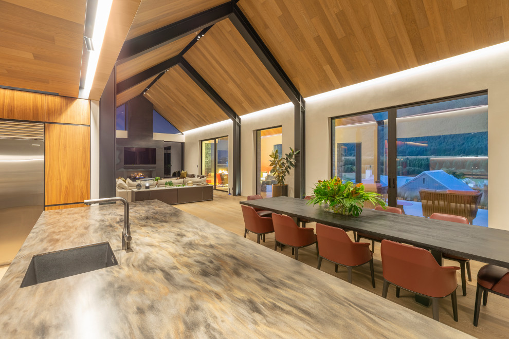 Expansive contemporary l-shaped open plan kitchen in Auckland with an undermount sink, flat-panel cabinets, black cabinets, solid surface benchtops, black appliances, light hardwood floors, with island, beige floor, multi-coloured benchtop, vaulted, grey splashback and porcelain splashback.
