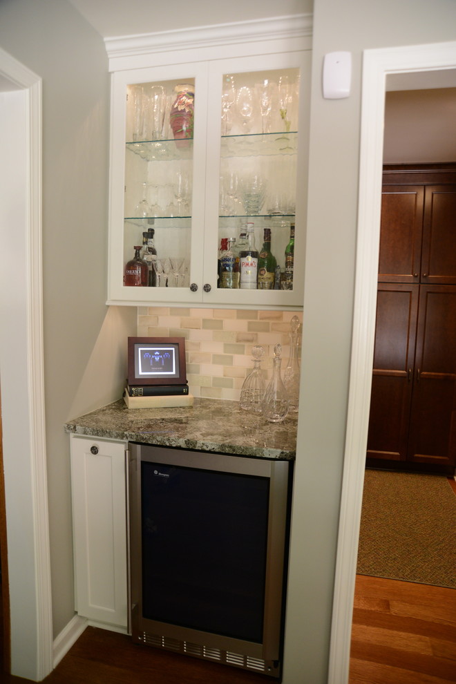 Home bar - transitional medium tone wood floor home bar idea in New York with shaker cabinets, white cabinets, granite countertops and beige backsplash