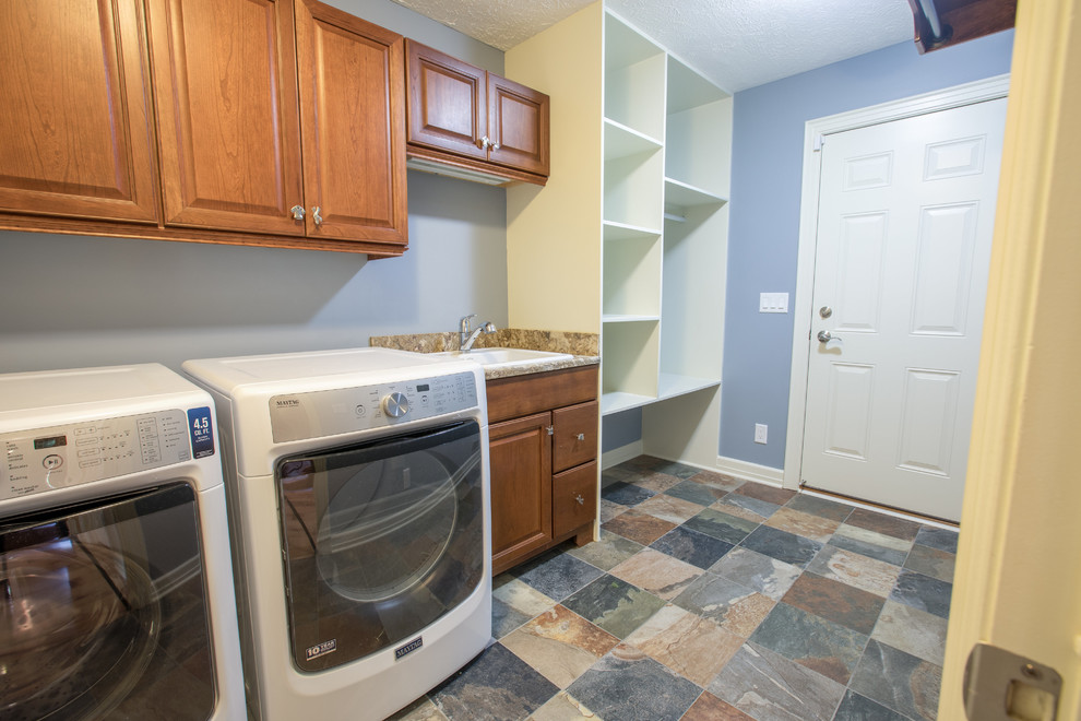 This is an example of a mid-sized transitional single-wall dedicated laundry room in Detroit with an undermount sink, raised-panel cabinets, medium wood cabinets, granite benchtops, blue walls, slate floors and a side-by-side washer and dryer.