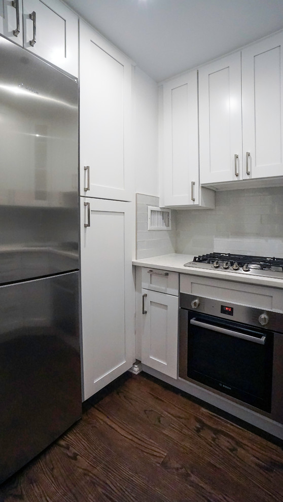 Small modern u-shaped eat-in kitchen in New York with a drop-in sink, shaker cabinets, white cabinets, quartz benchtops, white splashback, glass tile splashback, stainless steel appliances, dark hardwood floors, no island, brown floor and white benchtop.