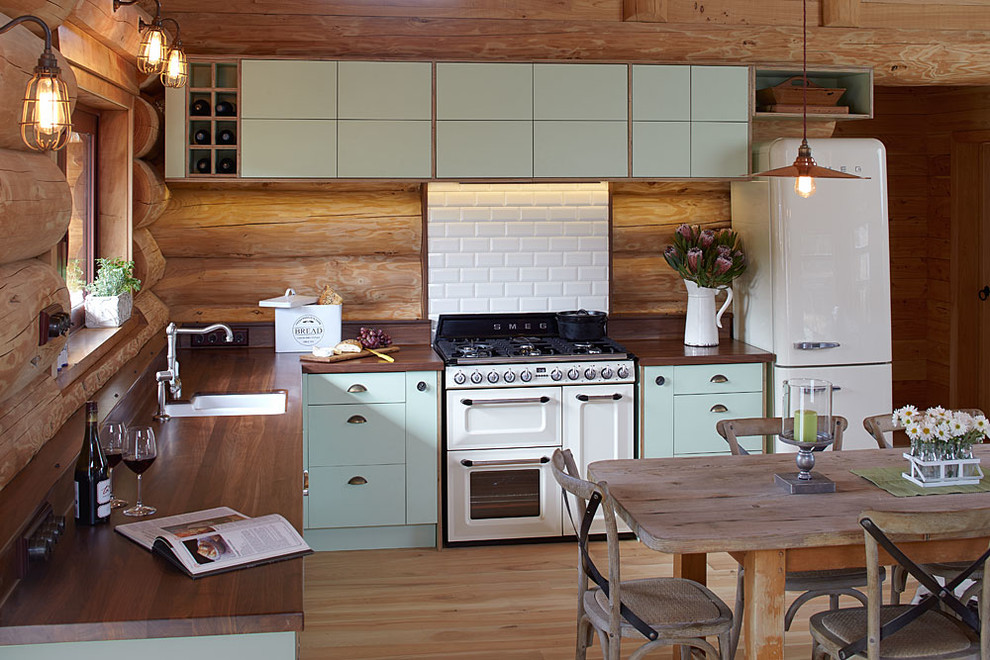 Mid-sized country l-shaped eat-in kitchen in Christchurch with a drop-in sink, flat-panel cabinets, green cabinets, wood benchtops, white splashback, ceramic splashback, white appliances, light hardwood floors and no island.