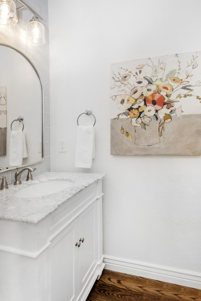 This is an example of a country powder room in Denver with recessed-panel cabinets, white cabinets, porcelain tile, white walls, medium hardwood floors, marble benchtops, brown floor, white benchtops and a freestanding vanity.