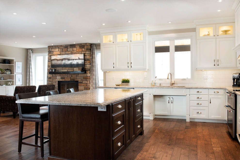 Inspiration for a large transitional l-shaped medium tone wood floor kitchen remodel in Toronto with an undermount sink, recessed-panel cabinets, white cabinets, quartz countertops, white backsplash, subway tile backsplash, stainless steel appliances and an island