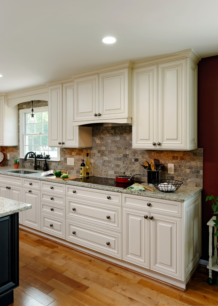 Photo of a large traditional galley eat-in kitchen in DC Metro with an undermount sink, raised-panel cabinets, white cabinets, granite benchtops, multi-coloured splashback, stone tile splashback, stainless steel appliances, with island, medium hardwood floors and brown floor.
