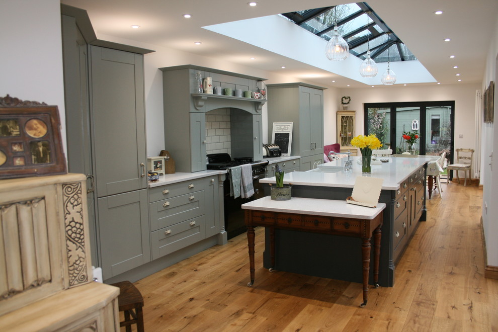 Large contemporary single-wall eat-in kitchen in Gloucestershire with shaker cabinets, grey cabinets, quartzite benchtops, light hardwood floors, with island, brown floor and subway tile splashback.