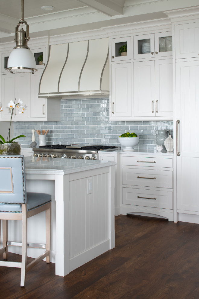 Large beach style galley open plan kitchen in Minneapolis with a farmhouse sink, shaker cabinets, white cabinets, quartzite benchtops, blue splashback, subway tile splashback, panelled appliances, medium hardwood floors, brown floor, white benchtop and timber.