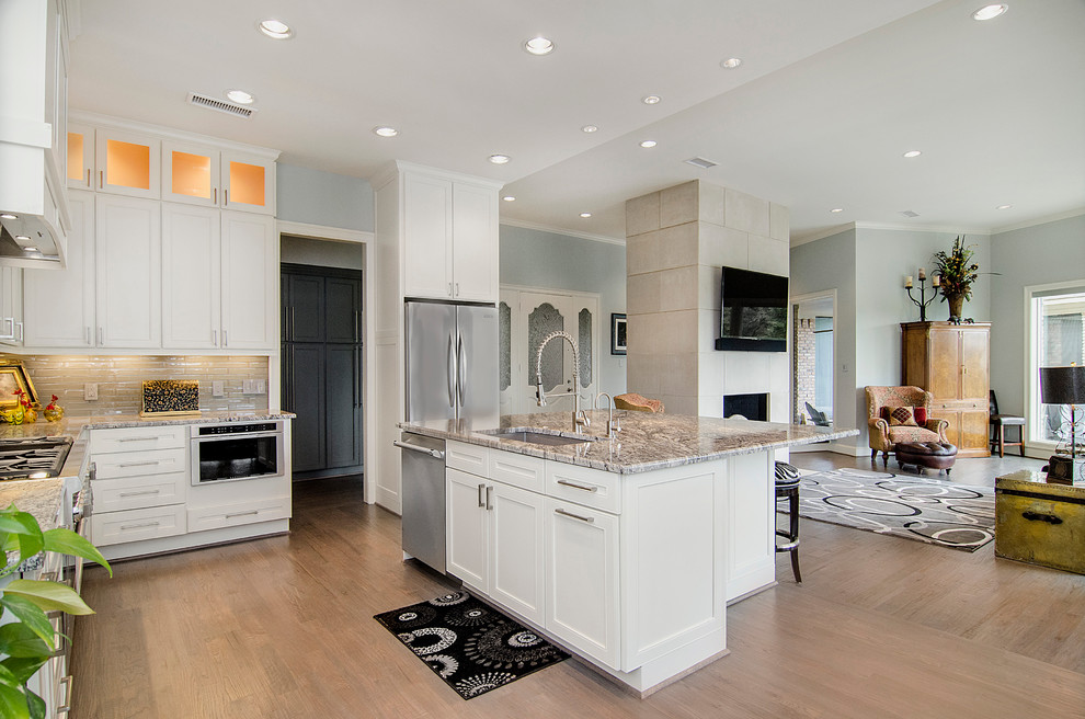 Inspiration for a mid-sized transitional l-shaped eat-in kitchen in Dallas with an undermount sink, shaker cabinets, white cabinets, granite benchtops, grey splashback, porcelain splashback, stainless steel appliances, medium hardwood floors and with island.