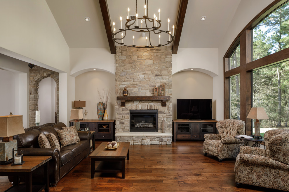 Photo of a mediterranean living room in Houston with dark hardwood floors, a standard fireplace, a stone fireplace surround and brown floor.