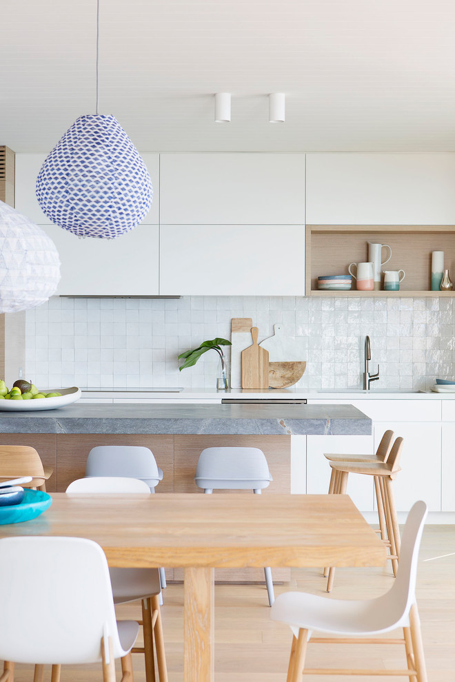 Photo of a large beach style galley open plan kitchen in Sydney with an undermount sink, flat-panel cabinets, white cabinets, quartz benchtops, white splashback, ceramic splashback, stainless steel appliances, light hardwood floors and with island.