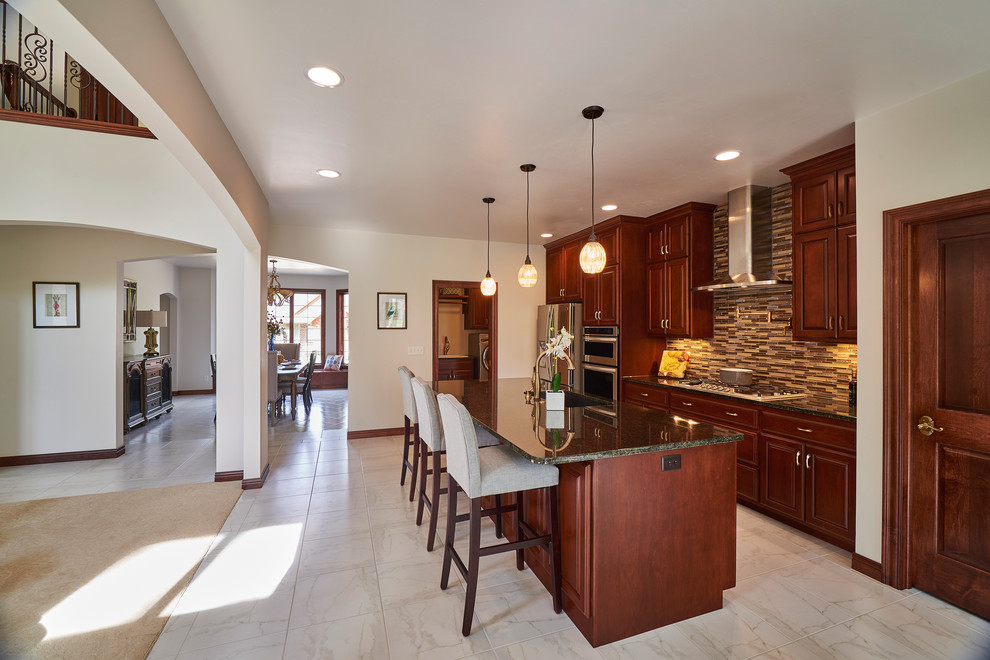 Mid-sized transitional galley porcelain tile and beige floor open concept kitchen photo with an undermount sink, raised-panel cabinets, dark wood cabinets, granite countertops, brown backsplash, mosaic tile backsplash, stainless steel appliances and an island