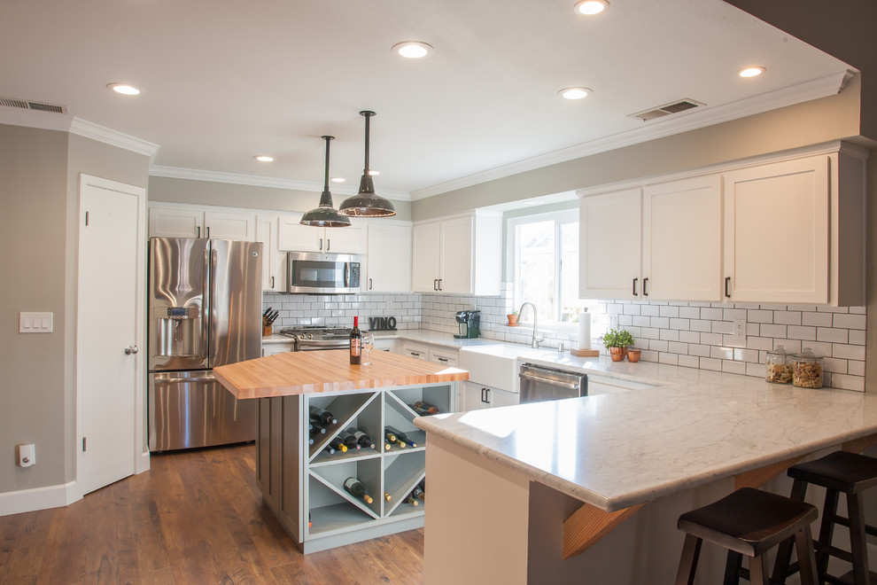 Photo of a mid-sized country u-shaped eat-in kitchen in Other with a farmhouse sink, shaker cabinets, white cabinets, marble benchtops, white splashback, subway tile splashback, stainless steel appliances, dark hardwood floors and with island.