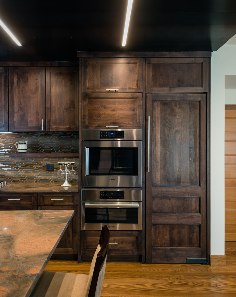 Example of a mid-sized minimalist galley medium tone wood floor and brown floor open concept kitchen design in Baltimore with an undermount sink, flat-panel cabinets, dark wood cabinets, granite countertops, brown backsplash, glass tile backsplash, an island and paneled appliances