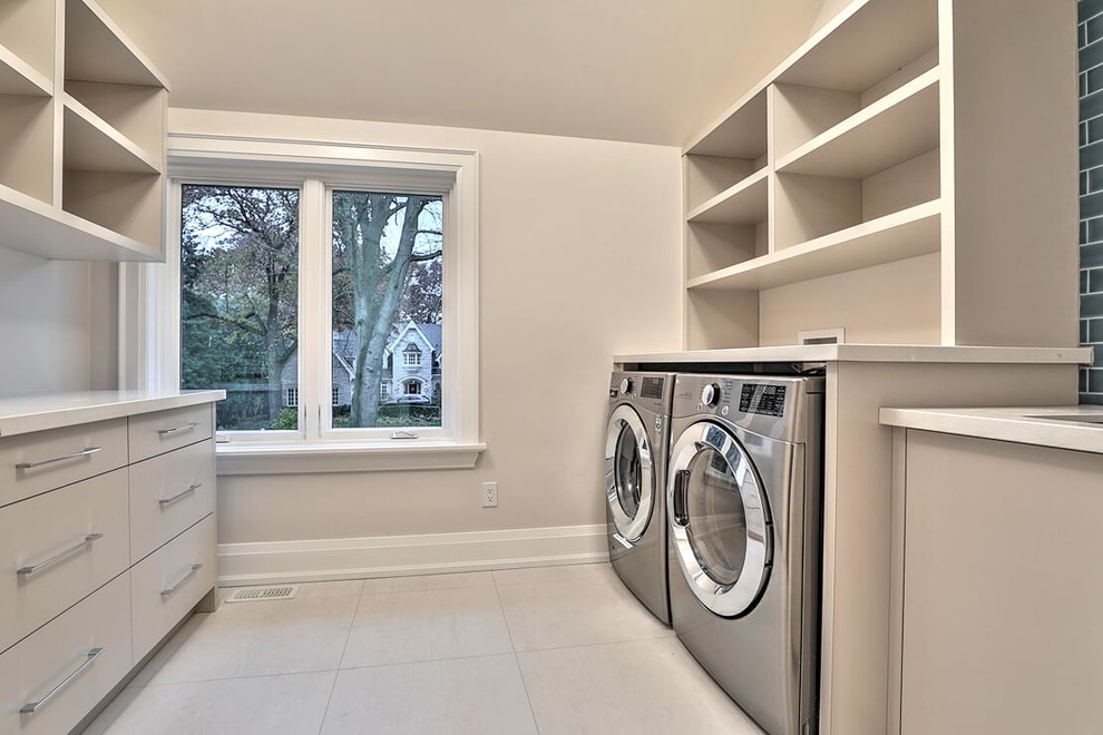 Design ideas for a large scandinavian galley dedicated laundry room in Toronto with a drop-in sink, flat-panel cabinets, beige cabinets, solid surface benchtops, beige walls, ceramic floors, a side-by-side washer and dryer, beige floor and beige benchtop.